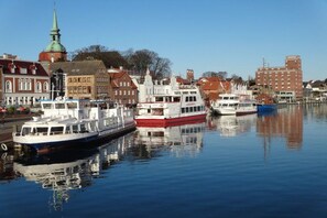 A calm river with several boats docked, a prominent church spire, and a mix of traditional and modern buildings along the riverbank. - Holiday apartment with 2 bedrooms (Kappeln Stadt)