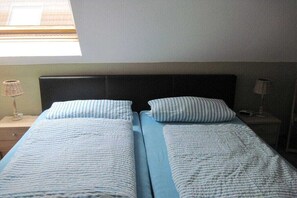 Une chambre avec deux lits, chacun agrémenté d’un oreiller à rayures et d’une couverture bleue. Il y a des tables de chevet avec des lampes.