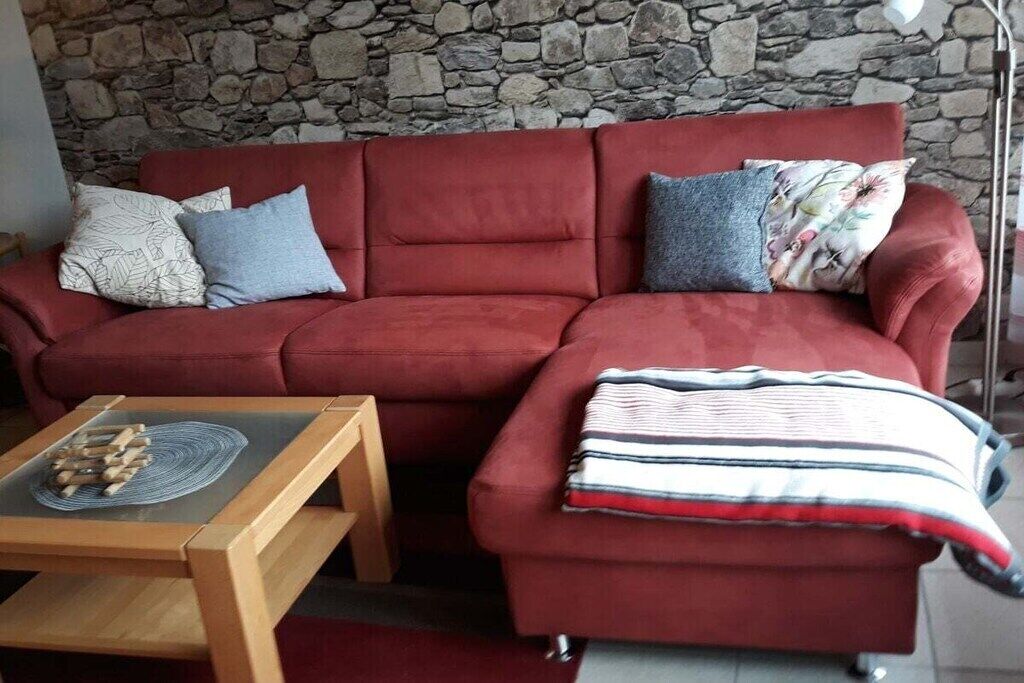 Ein rotes Sofa mit gemusterten Kissen, ein Holztisch und eine Steinwand im Hintergrund.