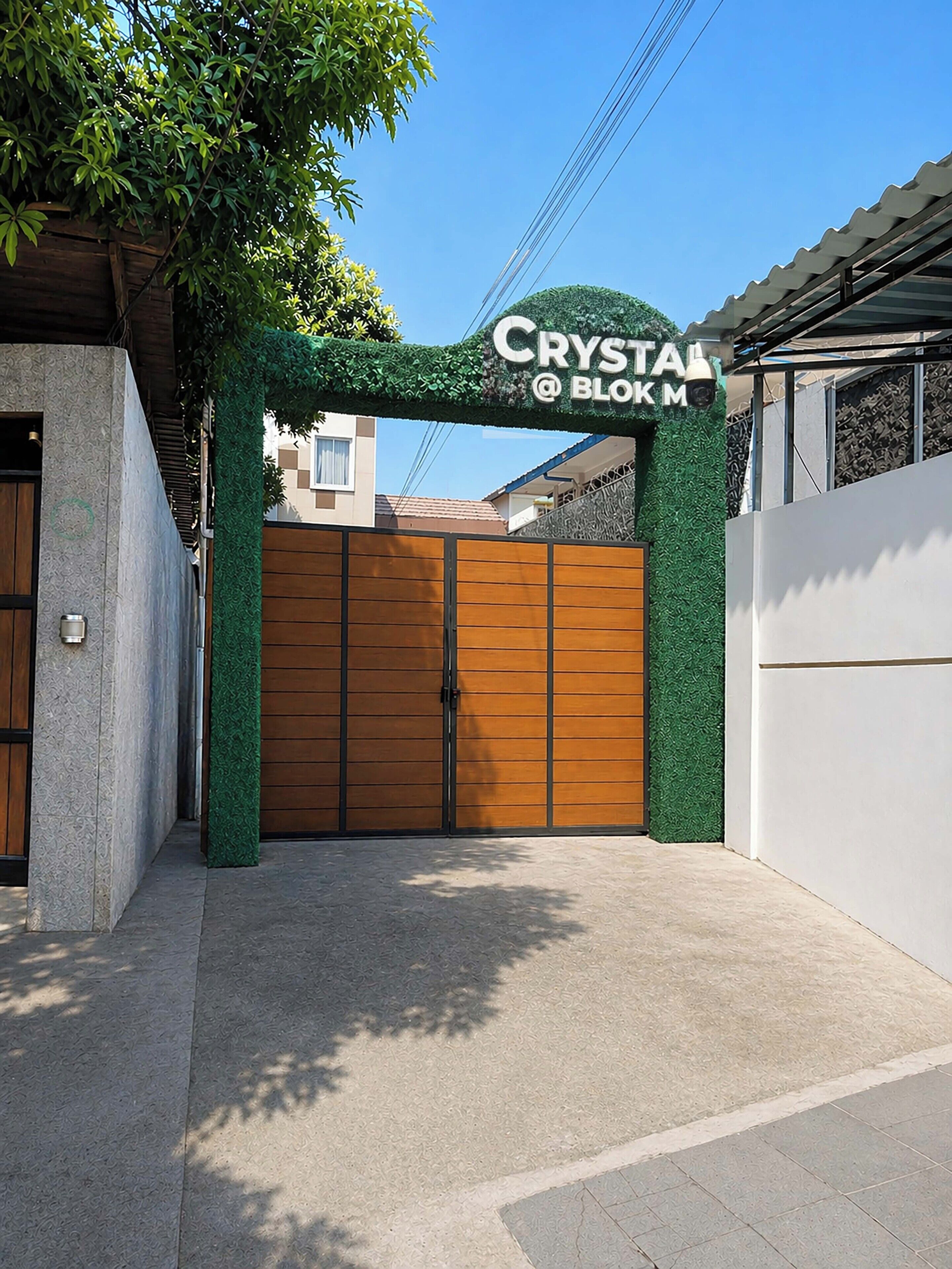 A gated entrance with a sign reading 'CRYSTAL @ BOKM' and a green wall with foliage.