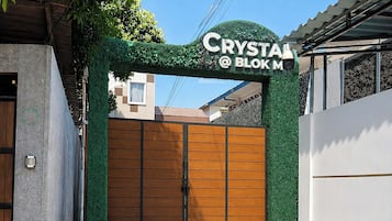 A gated entrance with a sign reading 'CRYSTAL @ BOKM' and a green wall with foliage.