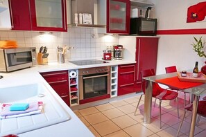 Een keuken met rode kasten, een magnetron, een oven en een eethoek met rode stoelen.