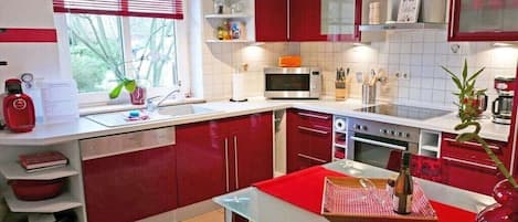Une cuisine moderne avec des meubles rouges, un four à micro-ondes, un four traditionnel et un coin repas avec une table rouge.