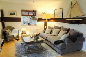 Ein Wohnzimmer mit Sofa, Sessel, Couchtisch, Lampe und einer Segelboot-Dekoration.