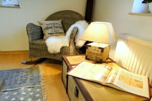 Ein gemütliches Zimmer mit einem Korbstuhl, einer Lampe und einem offenen Buch auf einem Holztisch.