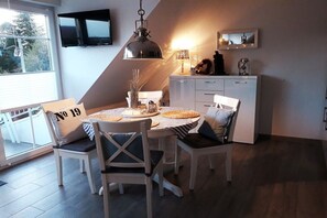 A dining area with a table set for four, a television mounted on the wall, and a kitchen area with cabinets and a countertop. - Holiday apartment with 2 bedrooms (Norden)