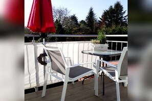 Une terrasse avec deux chaises blanches, une table en verre et un parasol rouge.