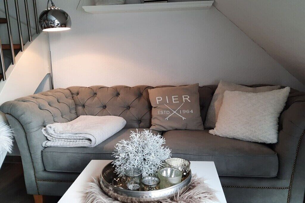 A grey tufted sofa with a white throw blanket and a decorative tray with a white tree-like ornament and candles.