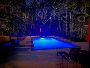 Une piscine éclairée de lumière bleue, entourée d’arbres et d’une clôture.