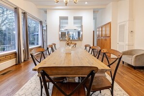 A dining room with a long wooden table, multiple chairs, a chandelier, and a view through large windows. - 6BR Fayetteville Retreat | Pool, Hot Tub & Pets (Fayetteville)