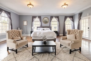 A bedroom with a large bed, two armchairs, a coffee table, and a chandelier. - 6BR Fayetteville Retreat | Pool, Hot Tub & Pets (Fayetteville)