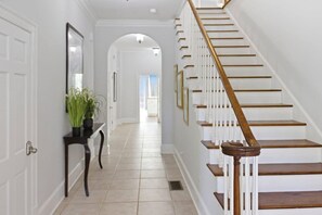 A hallway with a staircase, white walls, and a door on the left. - 6BR Fayetteville Retreat | Pool, Hot Tub & Pets (Fayetteville)