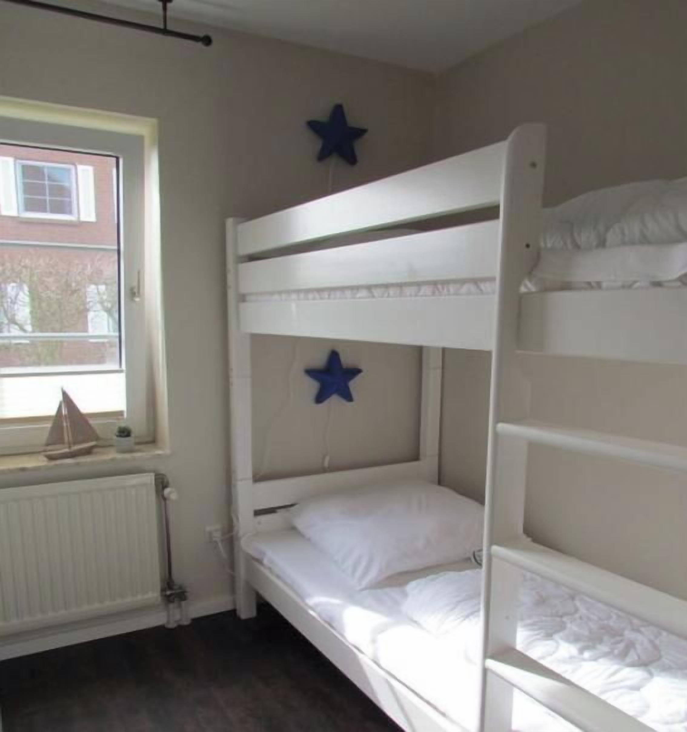 A bunk bed room with two stars on the wall, a window with a view of a building, and a radiator.