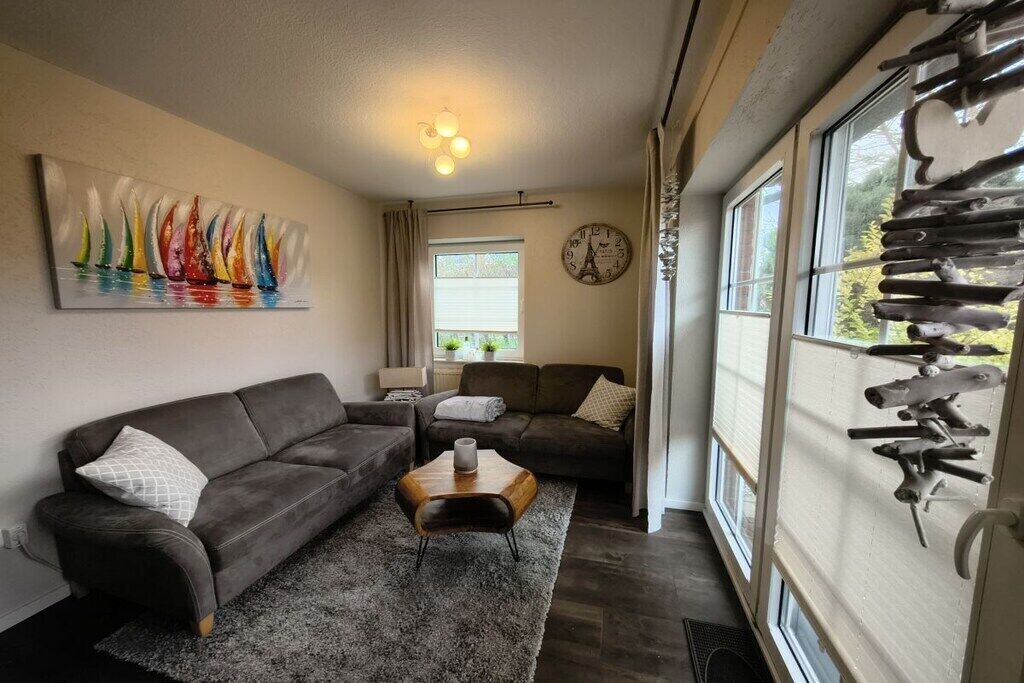 A living room with a sofa, a coffee table, a painting, a clock, and a window with curtains.