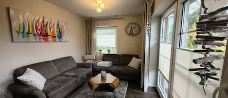 A living room with a sofa, a coffee table, a painting, a clock, and a window with curtains.