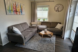 Een woonkamer met een bruine bank, een houten salontafel en een schilderij van zeilboten.