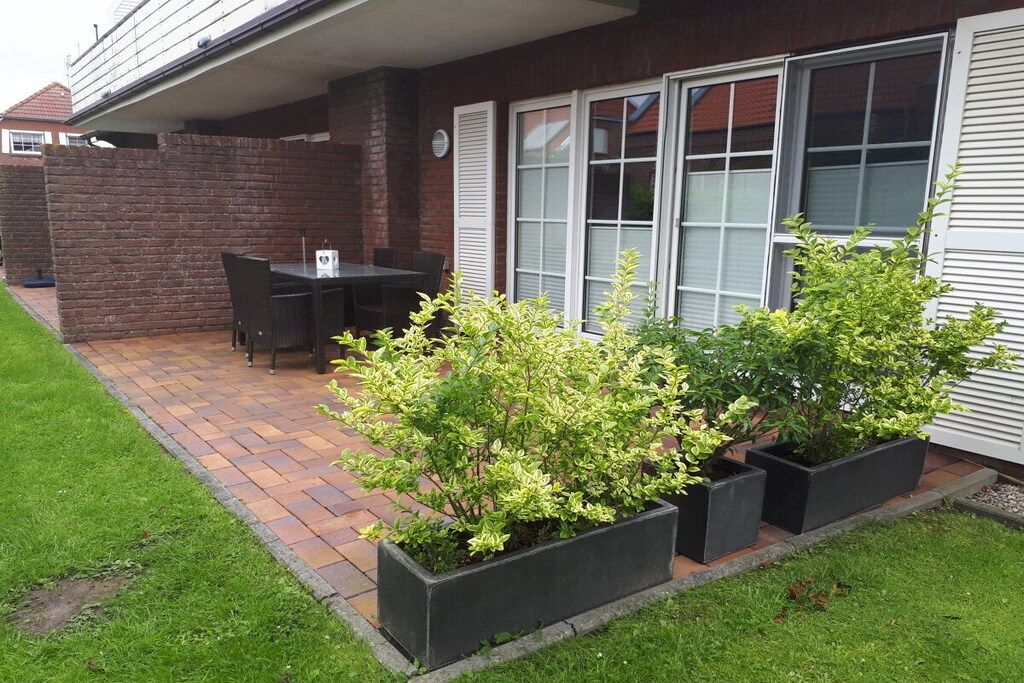 A patio with a table and chairs, surrounded by a brick wall and a grassy area.