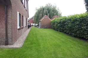 Een woonwijk met een verzorgd gazon, een huis met bakstenen gevel en luiken, en een fiets in de voortuin.