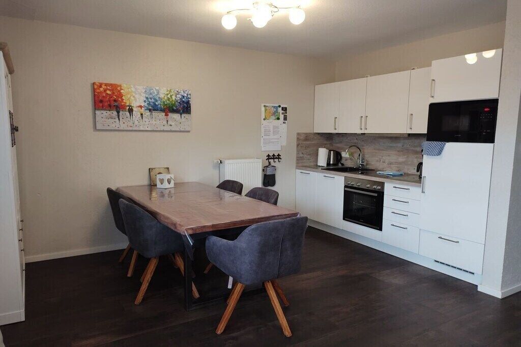 A modern kitchen with white cabinets, a wooden dining table, and a black microwave.