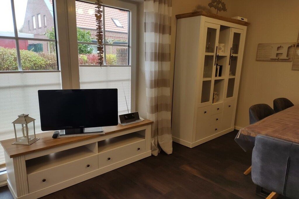 A living room with a TV on a wooden stand, a cabinet with glass doors, and a dining table with chairs.
