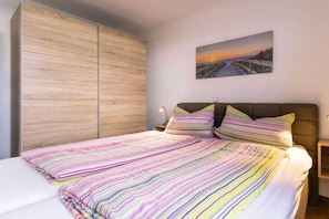 Une chambre à coucher avec un lit, une literie à rayures, une armoire en bois, une table de chevet et un tableau accroché au mur.