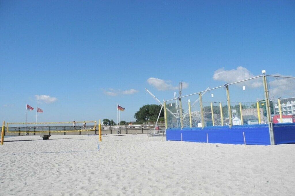 Cancha de voleibol de playa con red y líneas divisorias, rodeada de arena y un cielo despejado.
