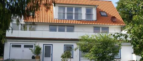A two-story residential building with a tiled roof, a front entrance, and a small garden area.