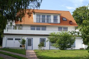 Ein zweigeschossiges Wohngebäude mit Ziegeldach, Hauseingang und kleinem Garten.