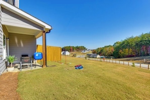 A residential backyard with a covered porch, a barbecue grill, a wooden fence, and a grassy lawn.