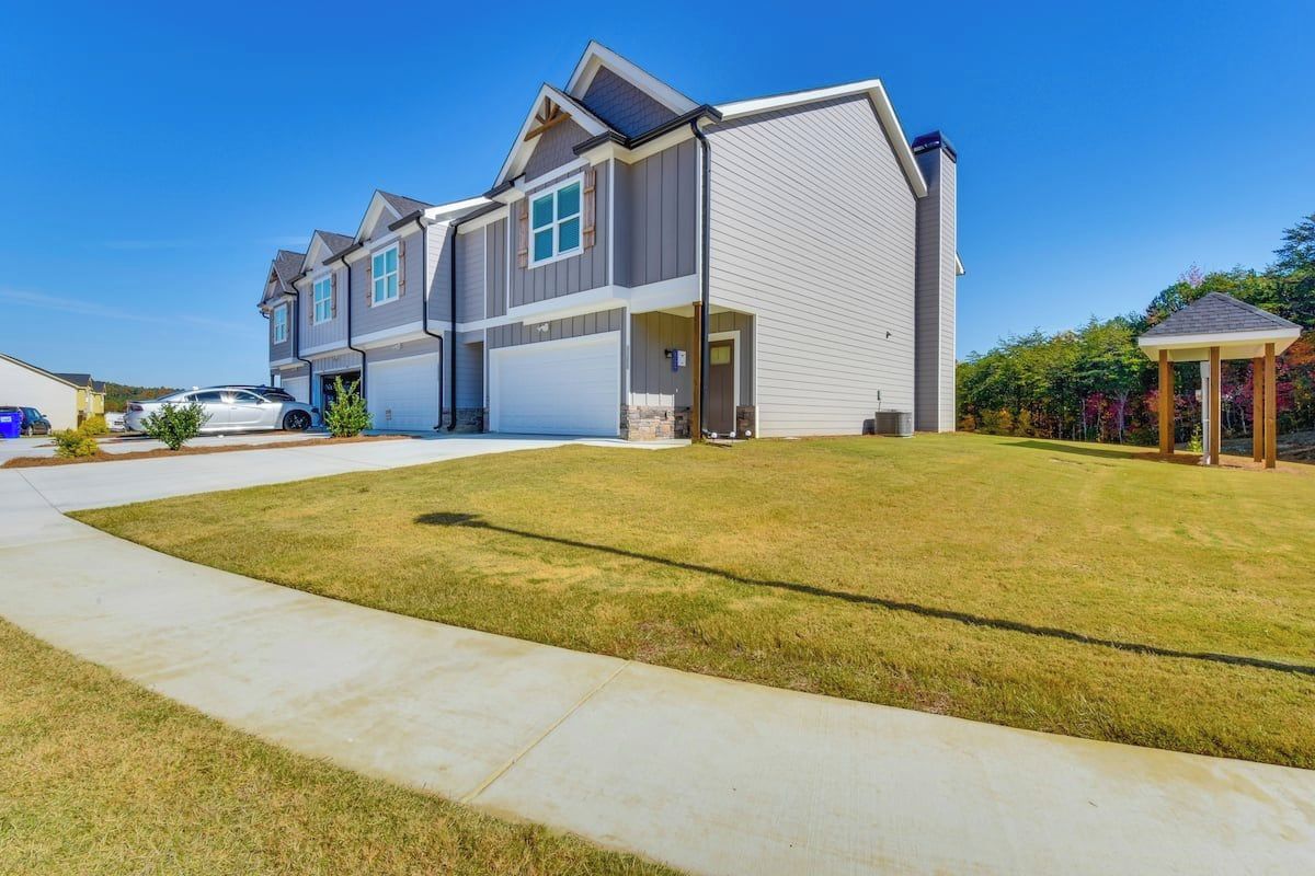 A two-story residential building with a garage, a covered porch, and a well-maintained lawn.