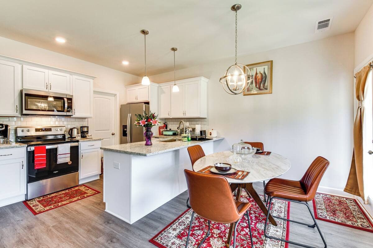 Ett modernt kök med vita skåp, rostfria vitvaror och en central köksö med sittplatser.