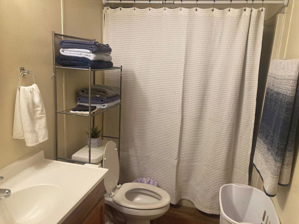 Une salle de bain comprenant des toilettes, un lavabo, une étagère avec des serviettes pliées et un rideau de douche.