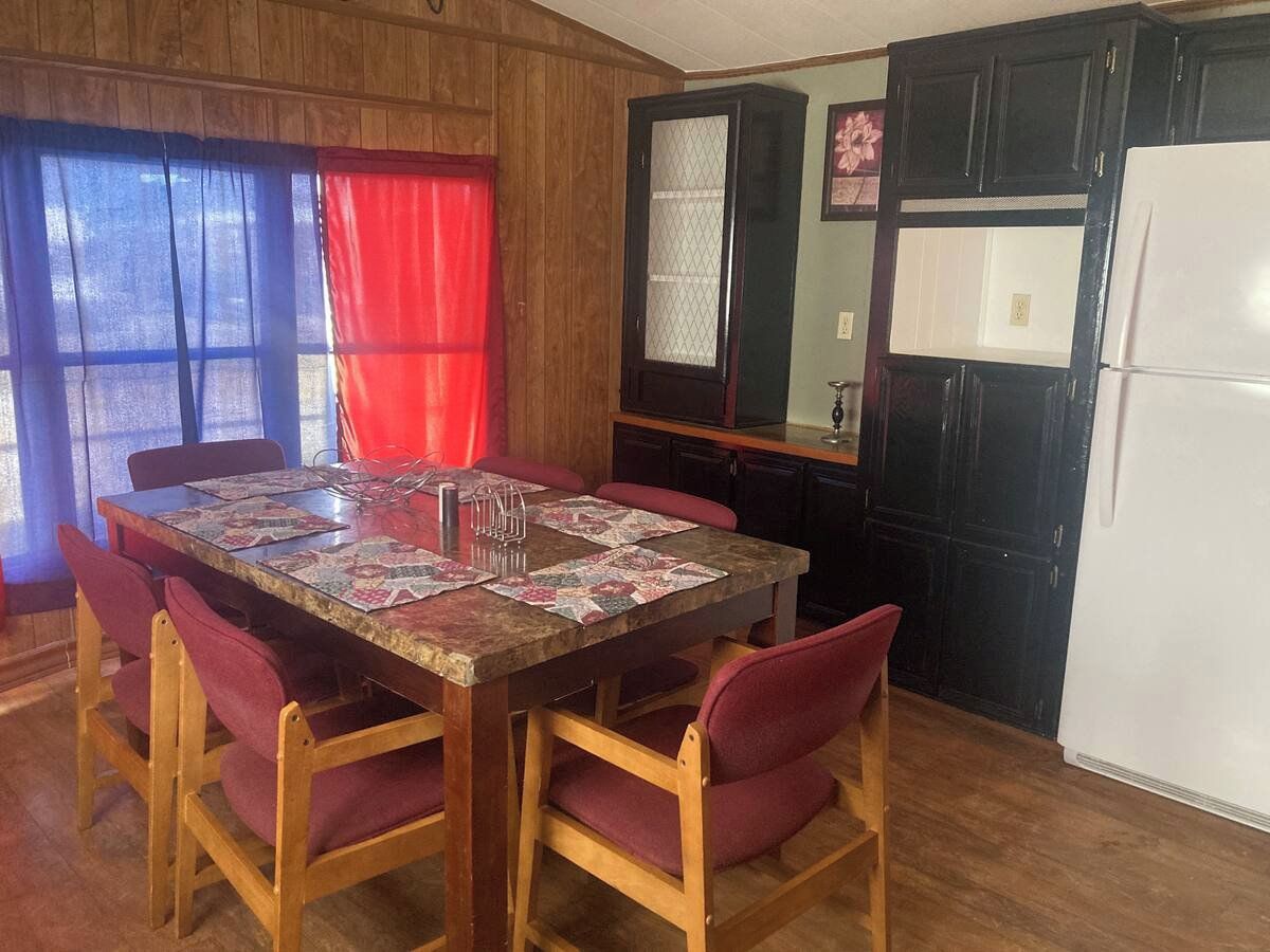 A dining area with a wooden table and red chairs, a refrigerator, and wooden cabinets.