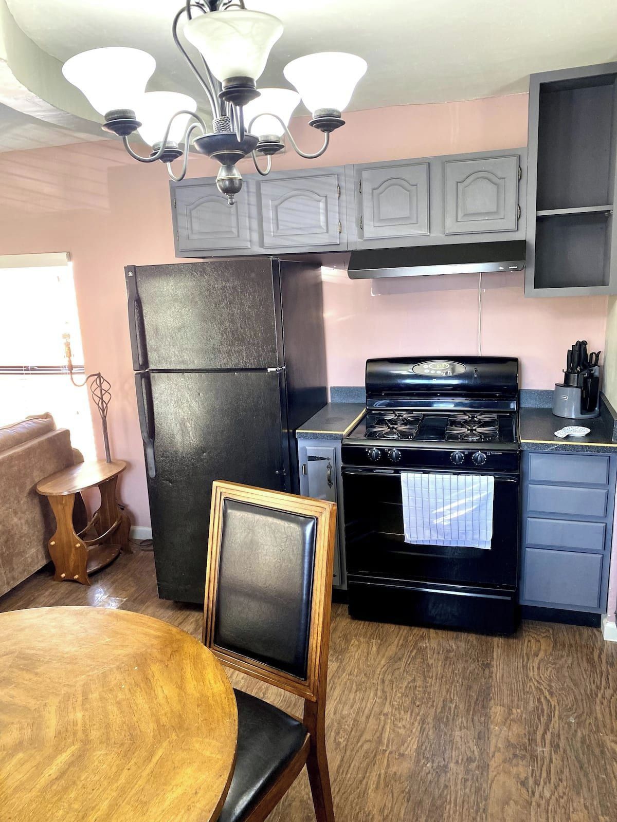 Une cuisine avec un réfrigérateur noir, une cuisinière et une table à manger avec une chaise.