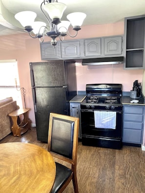 Une cuisine avec un réfrigérateur noir, une cuisinière et une table à manger avec une chaise.