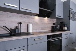 A modern kitchen with grey cabinetry, a wooden countertop, a black range hood, and a coffee maker. - Holiday apartment with 2 bedrooms (Carolinensiel)