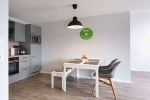 Une cuisine moderne avec des meubles gris, une table blanche et un luminaire suspendu noir.