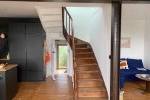 A modern interior with a wooden staircase, a kitchen with dark cabinets, and a blue sofa. - Cozy house between Trieux, GR34 & Bréhat (Lézardrieux)