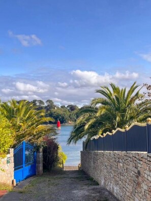 Un sentier mène à un plan d’eau, avec un mur de pierres et une porte bleue sur le côté gauche.