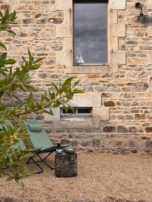 A stone building with a window, a small fire pit, and a green chair. - Cozy house between Trieux, GR34 & Bréhat (Lézardrieux)