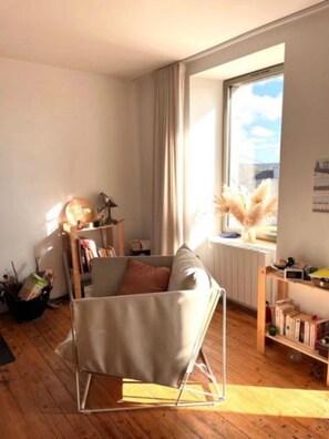 A modern living room with a minimalist sofa, a bookshelf, and a window with a view. - Cozy house between Trieux, GR34 & Bréhat (Lézardrieux)