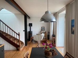 Un espace repas comprenant une table, des chaises, un vase de fleurs, un luminaire suspendu et un escalier.