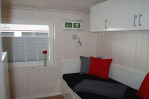 Een slaapkamer met een bed, een raam met zonwering, een wandlamp en een lijst met een afbeelding.
