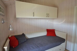 A single bed with a white headboard, a red pillow, a grey pillow, and a white cabinet above it. - Holiday home with 3 bedrooms (Wesselburenerkoog)