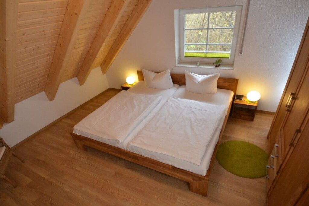 Un dormitorio con una cama de madera, dos mesitas de noche con lámparas, un ventanal con vistas y una alfombra verde.