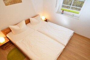 A double bed with white bedding, two bedside lamps, a small rug, and a window with a view of trees. - North Sea at Friesenhus Sellin (Ostseebad Sellin)