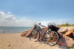 A bicycle with a basket and fenders parked on a sandy beach with large rocks, overlooking the sea. - Holiday home with 2 bedrooms (Neustadt\/Holstein - OT Pelzerhaken)