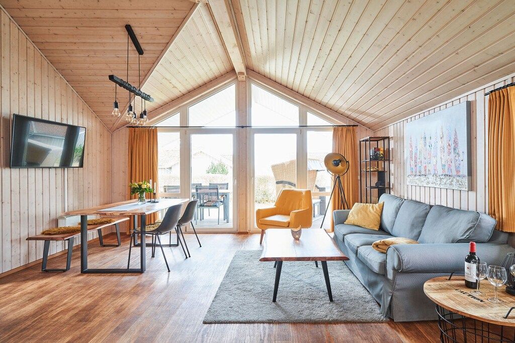 A modern interior with a wooden ceiling, a flat-screen TV, a dining area, a sofa, and a painting.