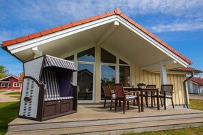 A covered outdoor seating area with a grill, a table with chairs, and a view of a house in the background. - Holiday home with 2 bedrooms (Neustadt\/Holstein - OT Pelzerhaken)