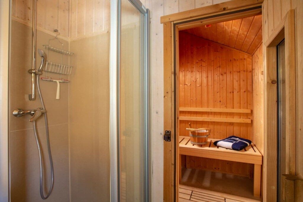 A wooden sauna with a glass door, a shower area with a hose, and a bench with a towel.